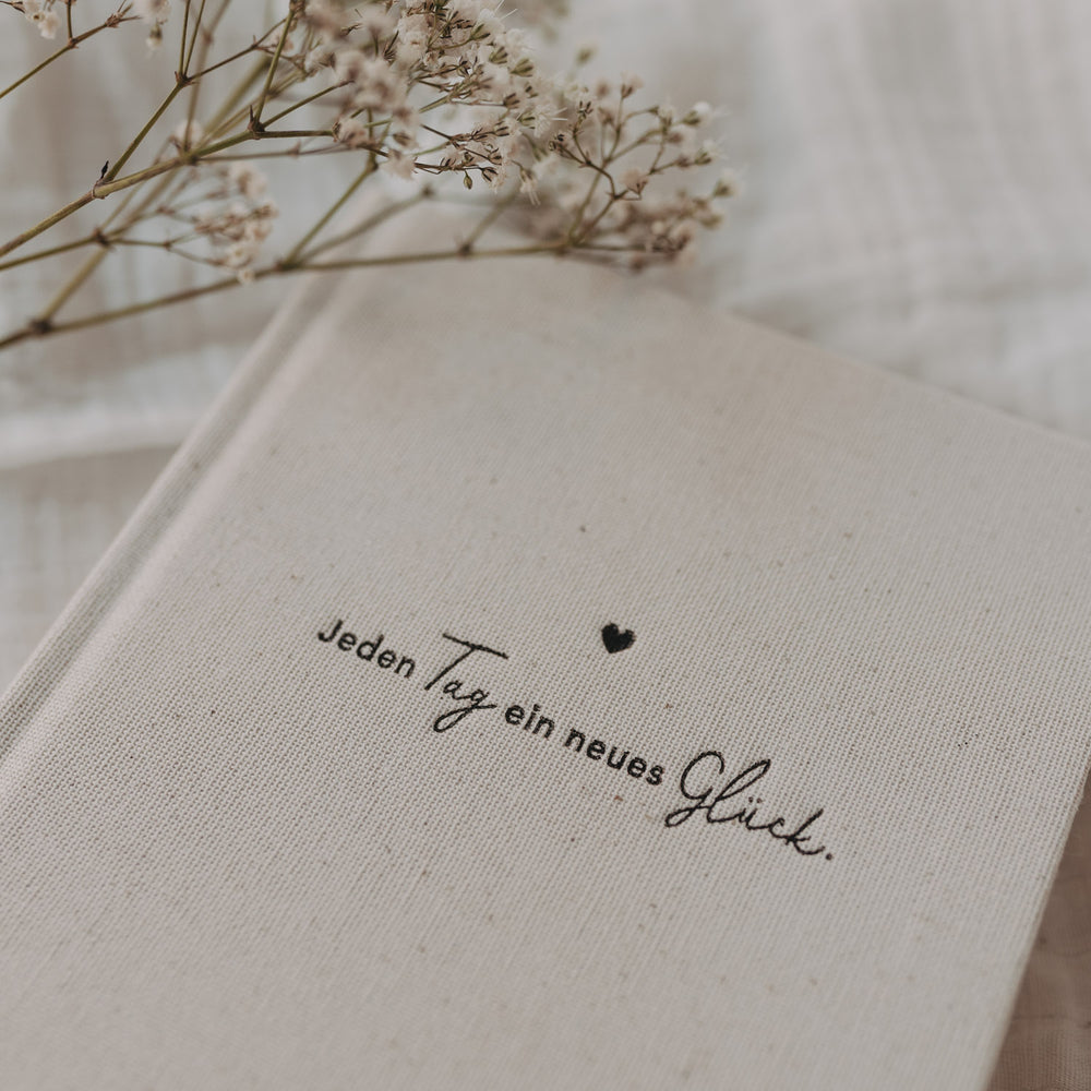 Detailaufnahme des Kalenders „Neues Glück“ mit Strukturcover und Schriftzug, dekoriert mit zarten Trockenblumen.