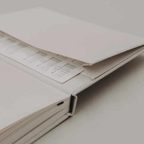 Offene Kalenderinnenseite mit Einstecktasche und eingelegter Jahresübersicht im Kalender „Neues Glück“.