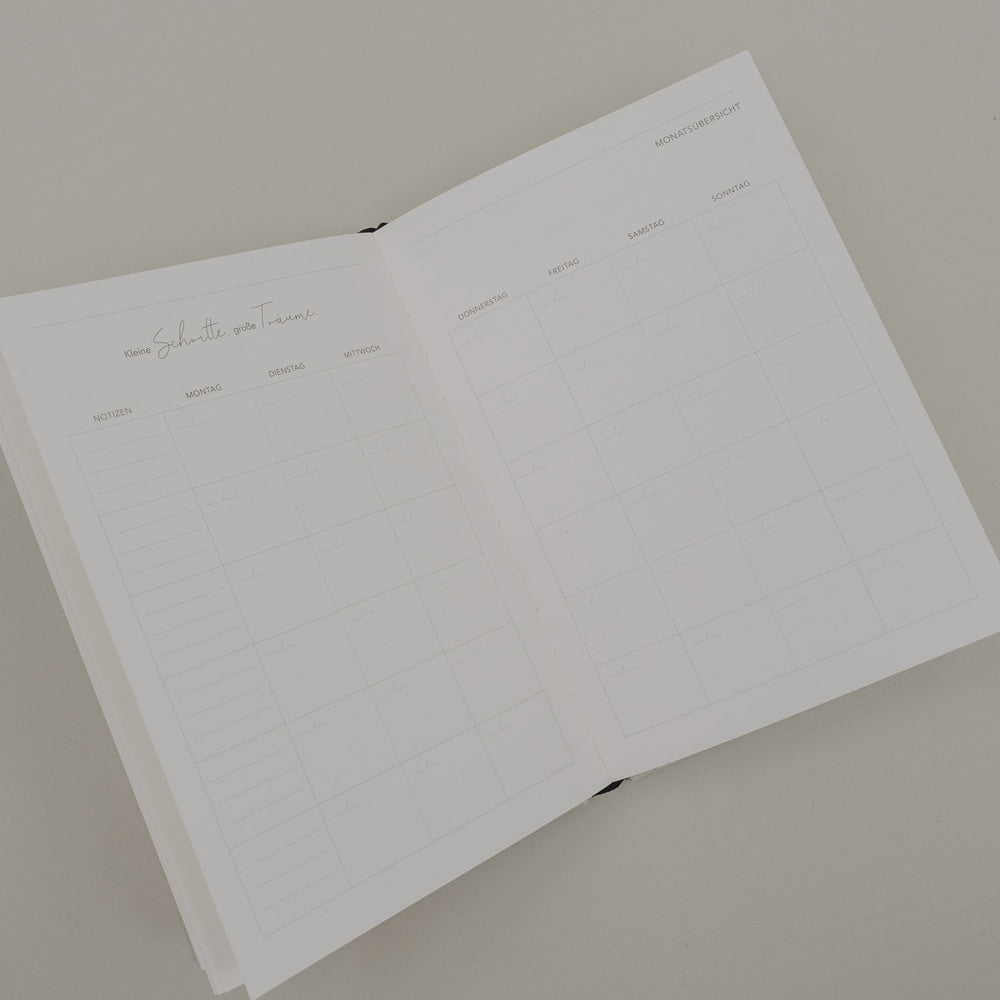 Geöffneter Kalender „Neues Glück“ mit Monatsübersicht und Wochenfeldern im schlichten, minimalistischen Design