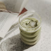 Glas mit grünem Matcha und sternförmigem Eiswürfel auf hellem Tisch, dekorativ inszeniert mit offenem Buch im Hintergrund.