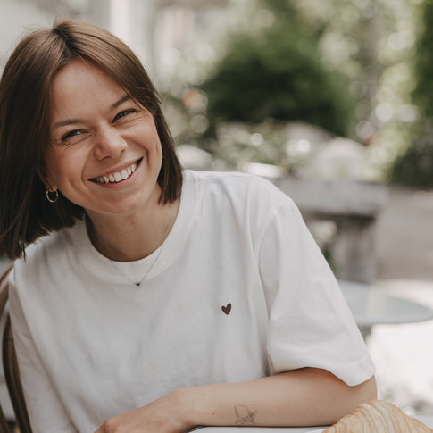 Frau mit weißem T-Shirt mit kleinem Herz-Print lächelt im Café