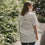 Frau im weißen T-Shirt mit Kaffee-Print spaziert im Grünen