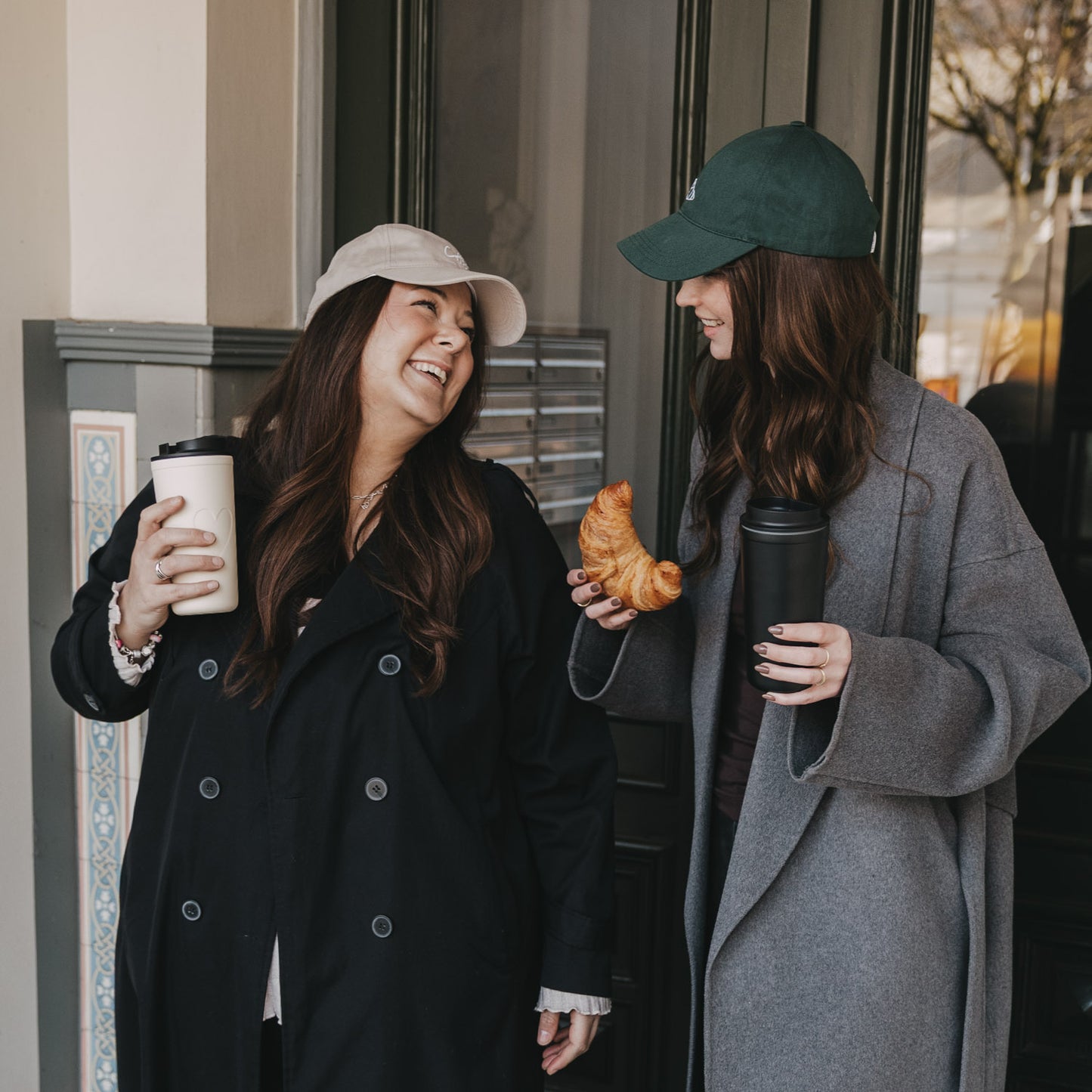 Zwei Frauen mit Caps und Coffee-to-go, eine trägt dunkelgrüne „Breakfast Club“ Cap
