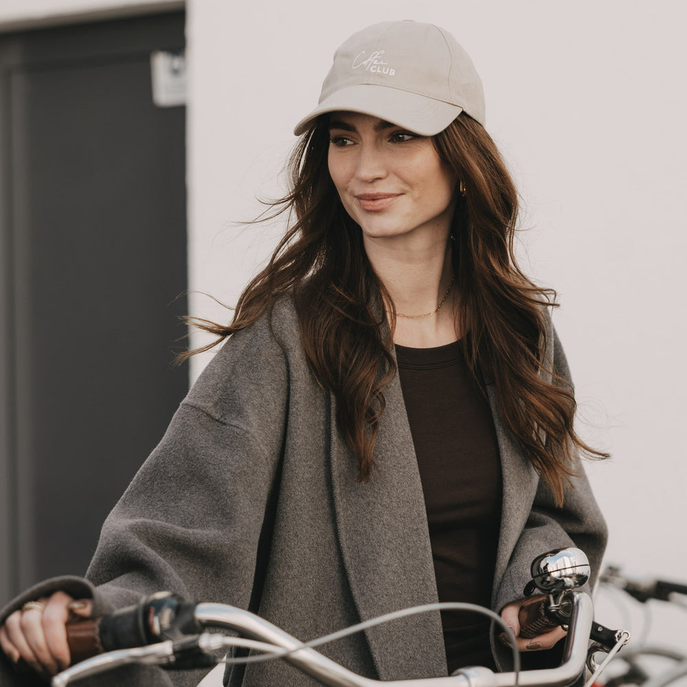 Frau mit taupefarbener „Coffee Club“ Cap fährt Fahrrad