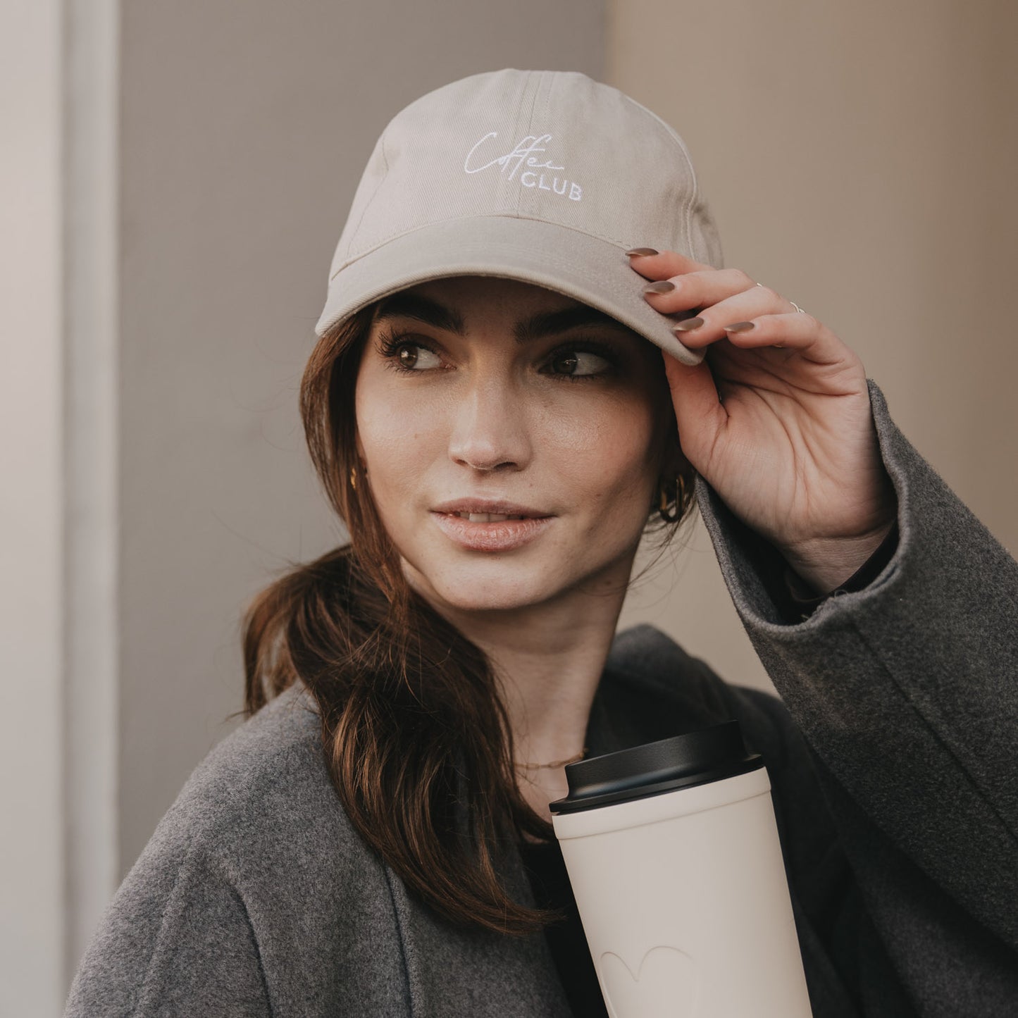 Frau mit taupefarbener „Coffee Club“ Cap und Coffee-to-go Becher