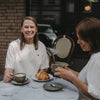 Zwei Frauen im Café mit Kaffee, eine trägt weißes T-Shirt mit kleinem Herz-Print