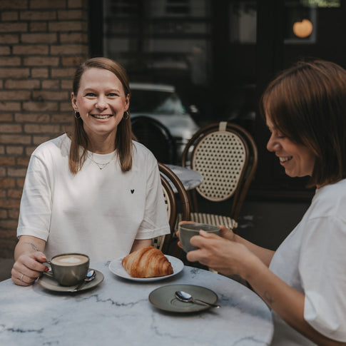 Zwei Frauen im Café mit Kaffee, eine trägt weißes T-Shirt mit kleinem Herz-Print