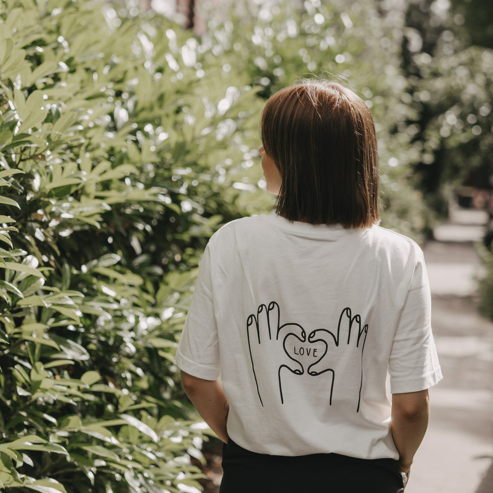 Frau mit weißem T-Shirt und LOVE-Print auf dem Rücken blickt zurück