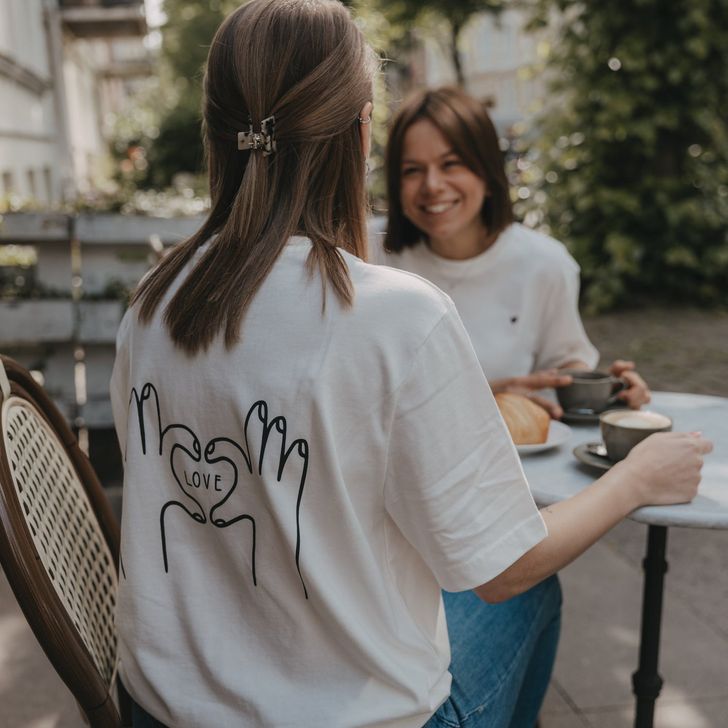Rückansicht T-Shirt mit LOVE-Print aus Händen, Frau sitzt im Café