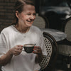 Frau im weißen T-Shirt mit Herz-Print trinkt Kaffee im Café