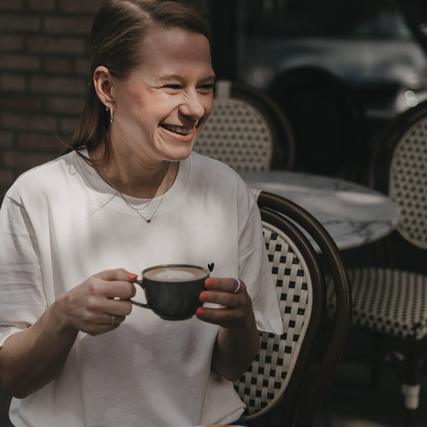 Frau im weißen T-Shirt mit Herz-Print trinkt Kaffee im Café