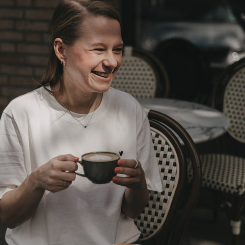 Frau im weißen T-Shirt mit Herz-Print trinkt Kaffee im Café
