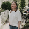 Frau im weißen T-Shirt mit Herz-Print steht lächelnd im Grünen