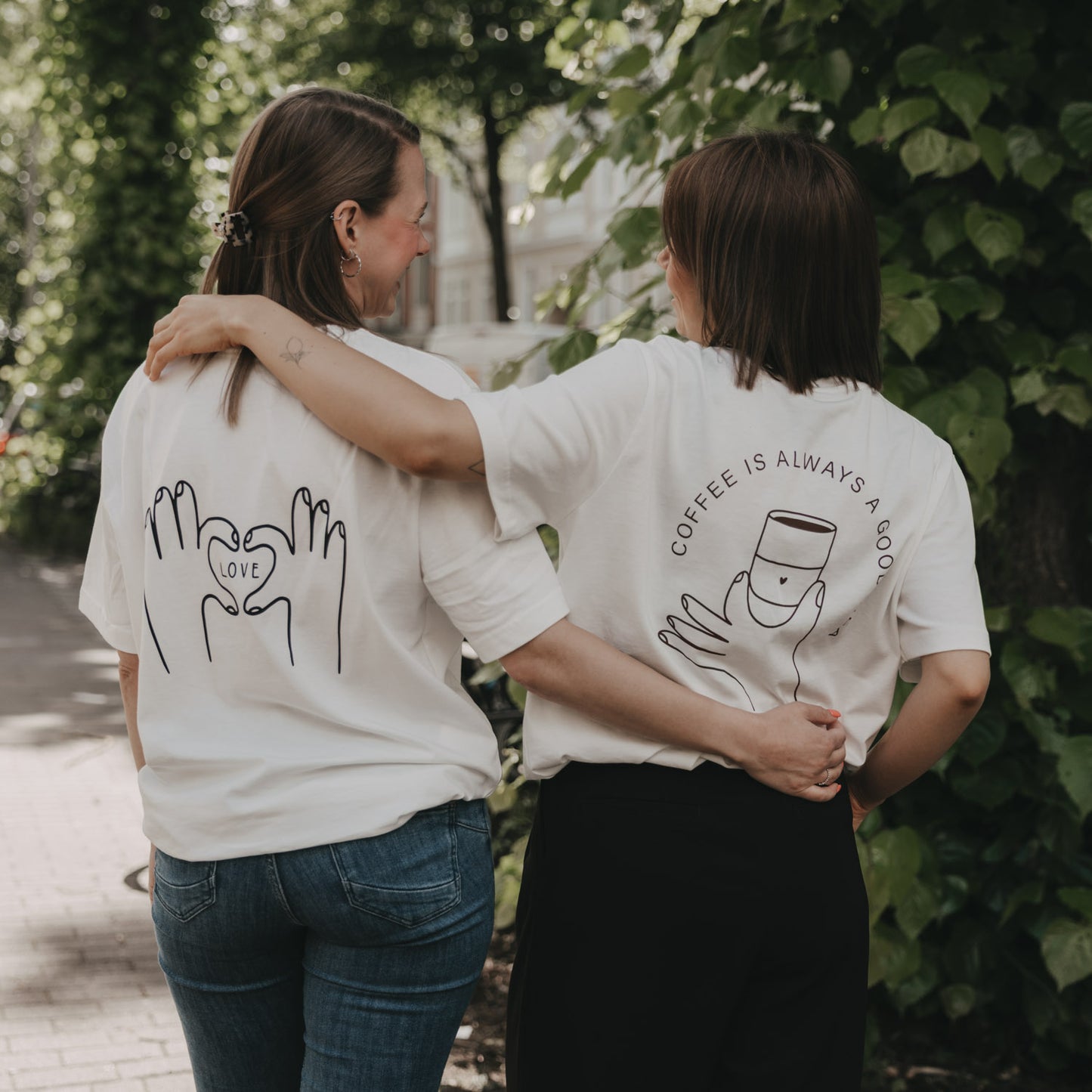Zwei Frauen in T-Shirts mit LOVE- und Kaffee-Print, Rückenansicht im Grünen