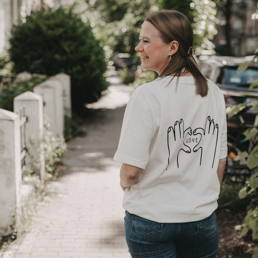 Frau trägt weißes T-Shirt mit LOVE-Print auf dem Rücken, draußen fotografiert