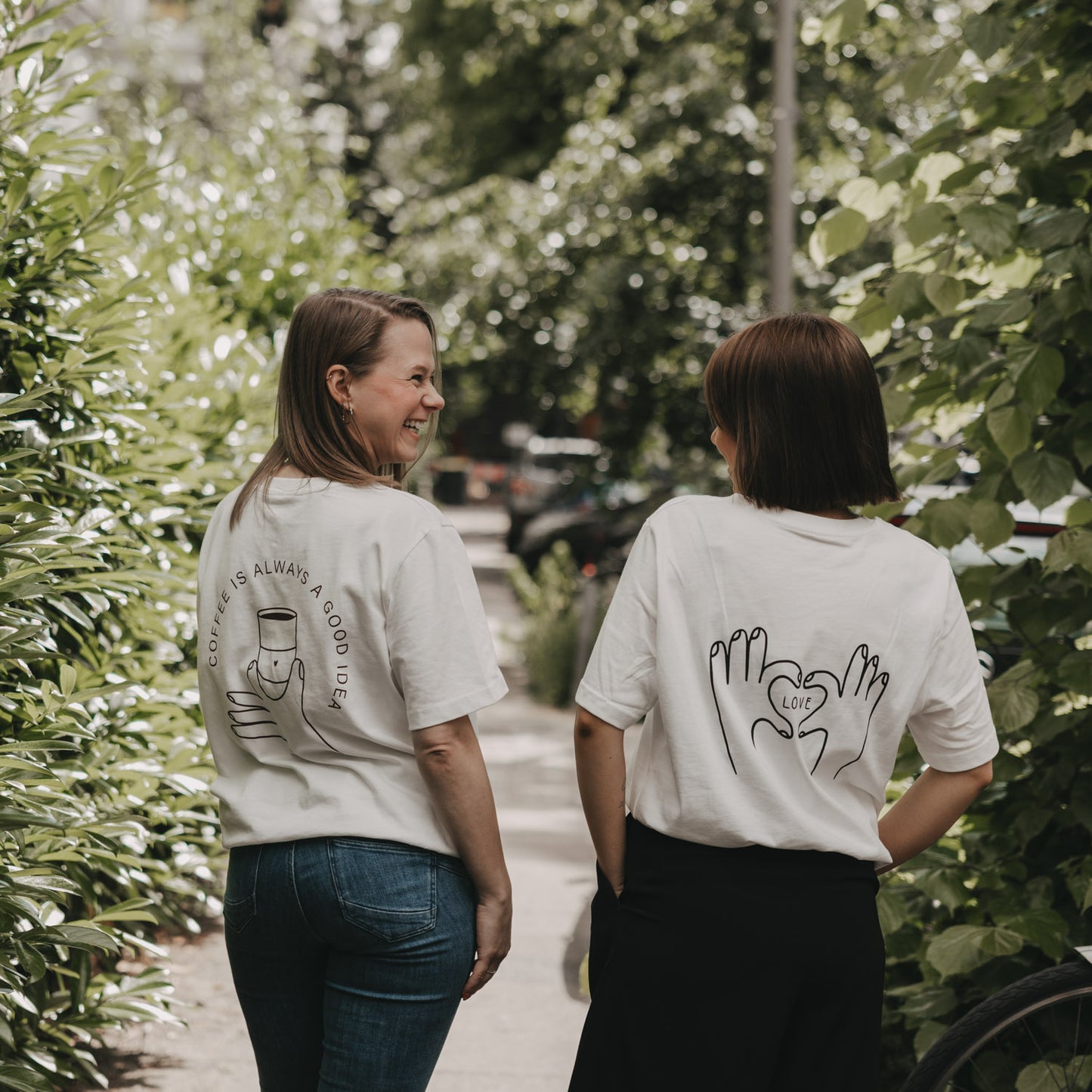 Zwei Frauen in T-Shirts mit LOVE- und Kaffee-Print, Rückenansicht im Grünen