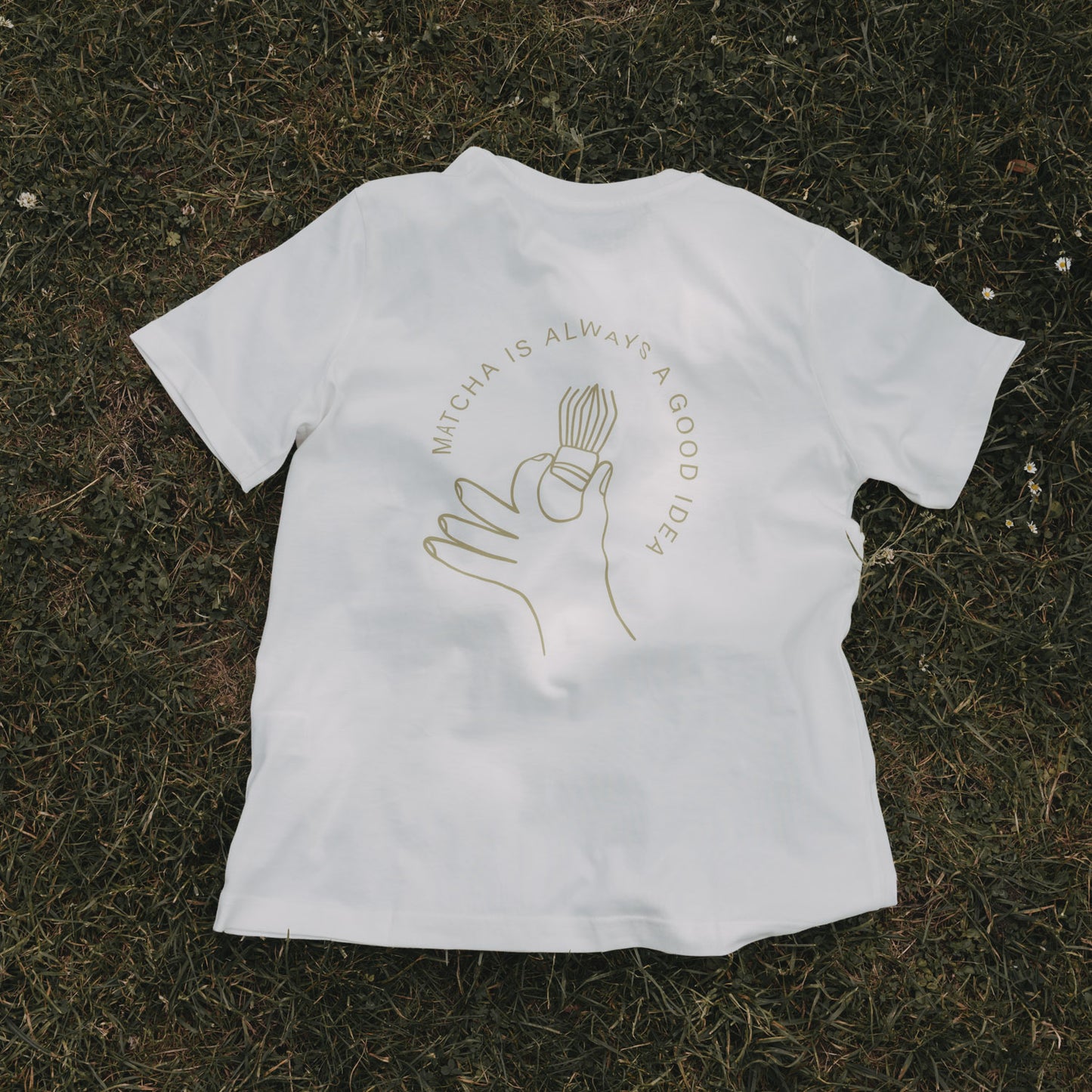 Weißes Matcha T-Shirt flach auf Gras liegend, mit Print im Fokus