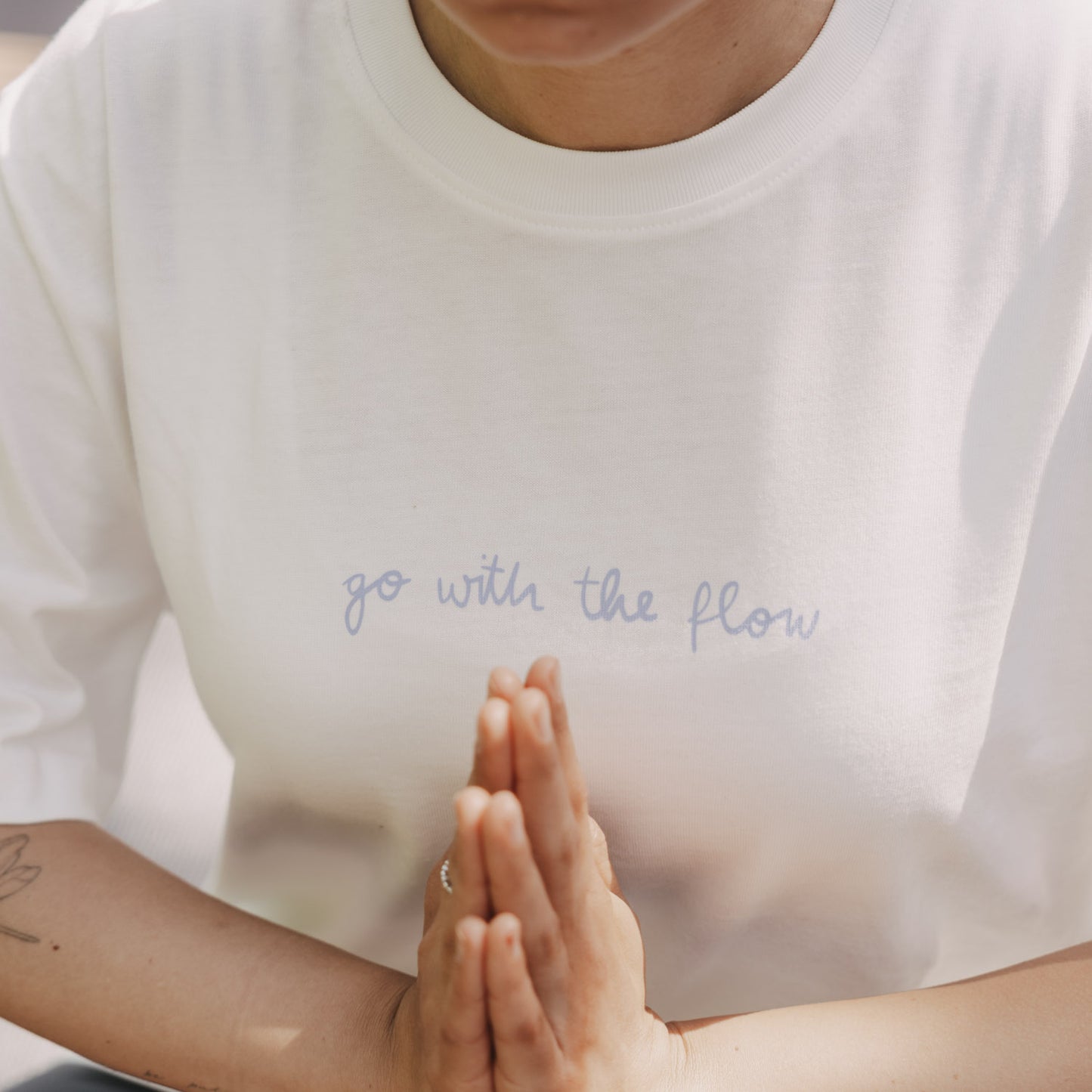 Detailansicht: weißes T-Shirt mit Schriftzug „go with the flow“ vorne, Hände in Gebetshaltung