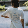Rückenansicht weißes T-Shirt mit „Ocean Child“ Print und Meeresillustrationen am Wasser