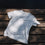 Weißes „Ocean Child“ T-Shirt flach auf Holzsteg liegend, minimalistische Produktansicht