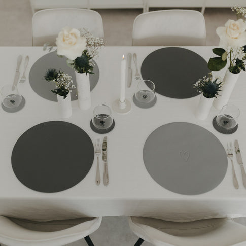 Gesamtansicht eines gedeckten Tisches mit grauen Platzsets und weißen Blumenvasen.