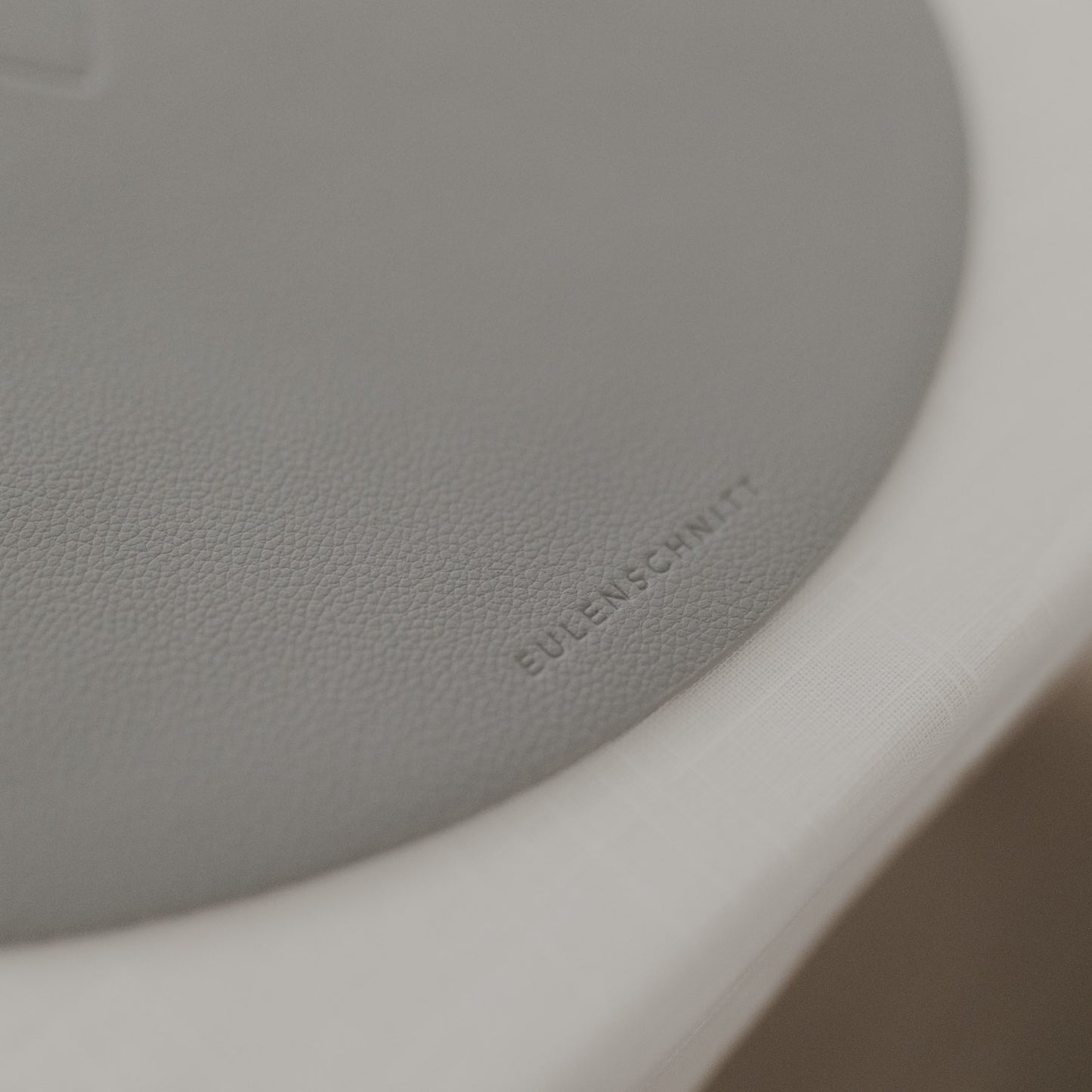 Detailaufnahme des hellgrauen Platzsets mit eingeprägtem Eulenschnitt-Logo auf weißer Tischdecke.