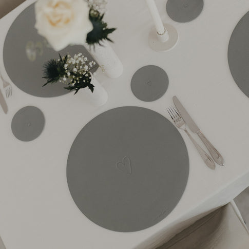 Tischansicht mit grauem Platzset und Untersetzer mit eingeprägtem Herzmotiv.