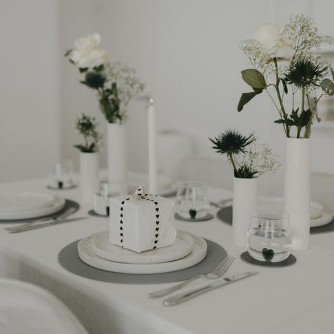 Tischdekoration mit grauem Platzset und weißem Geschirr sowie Geschenkpaket auf dem Teller.