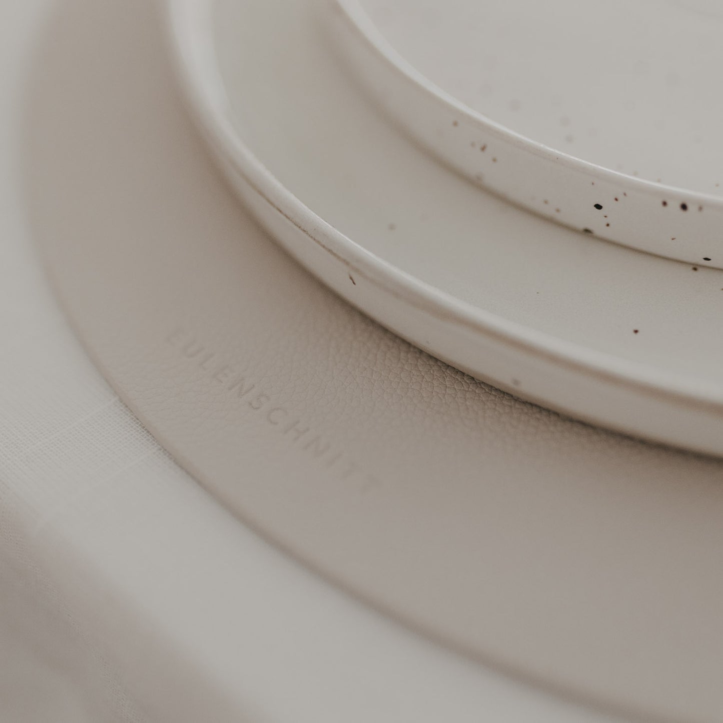 Detailaufnahme: Eulenschnitt-Prägung auf cremefarbenem, rundem Platzset.