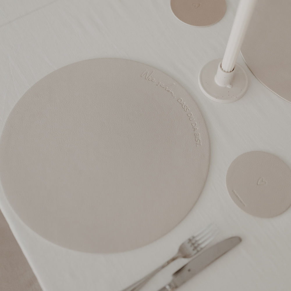 Cremefarbenes Platzset mit Prägung „Wie schön, dass du da bist“ auf gedecktem Tisch.