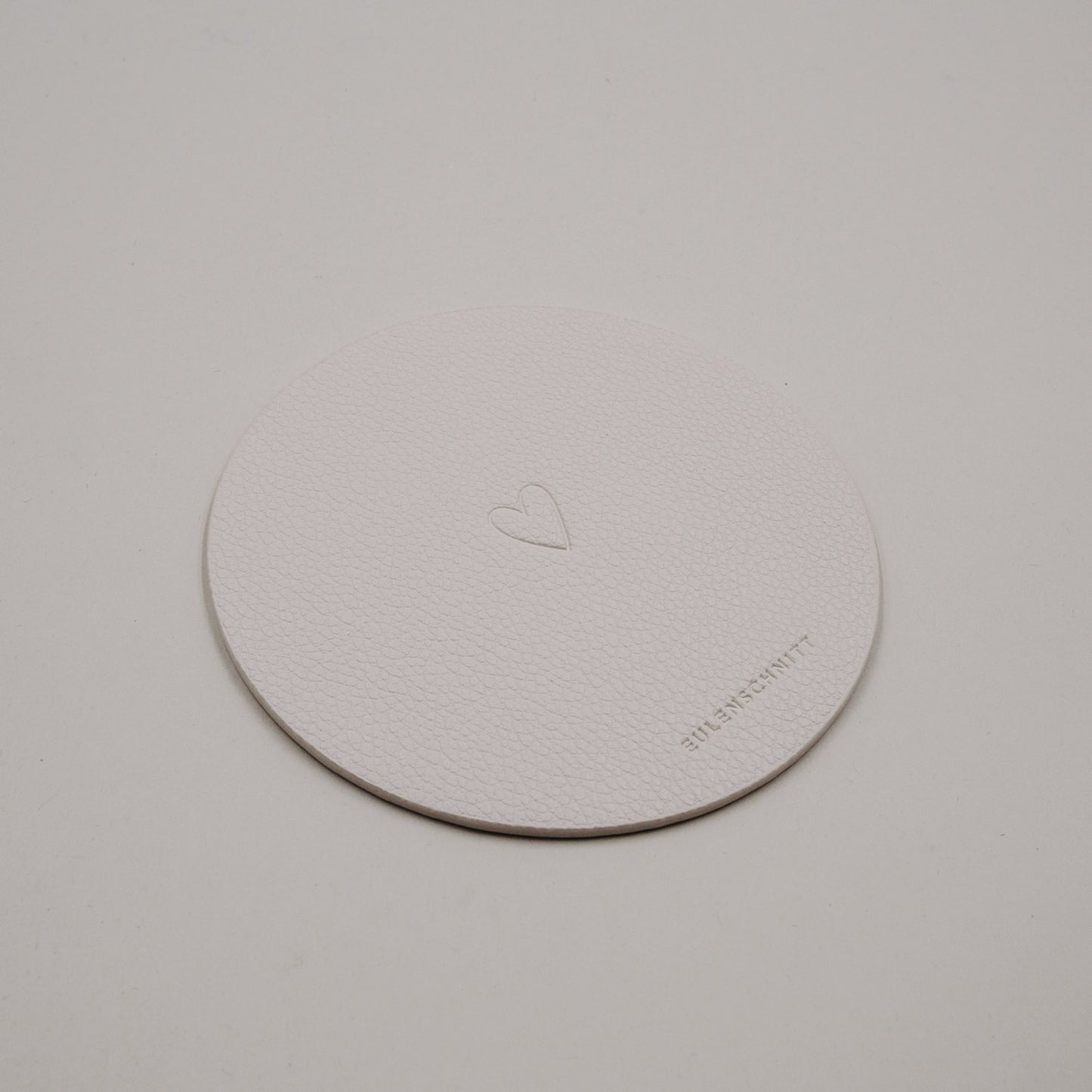 Heller runder Untersetzer aus Kunstleder in Creme mit eingeprägtem Herzmotiv von Eulenschnitt.