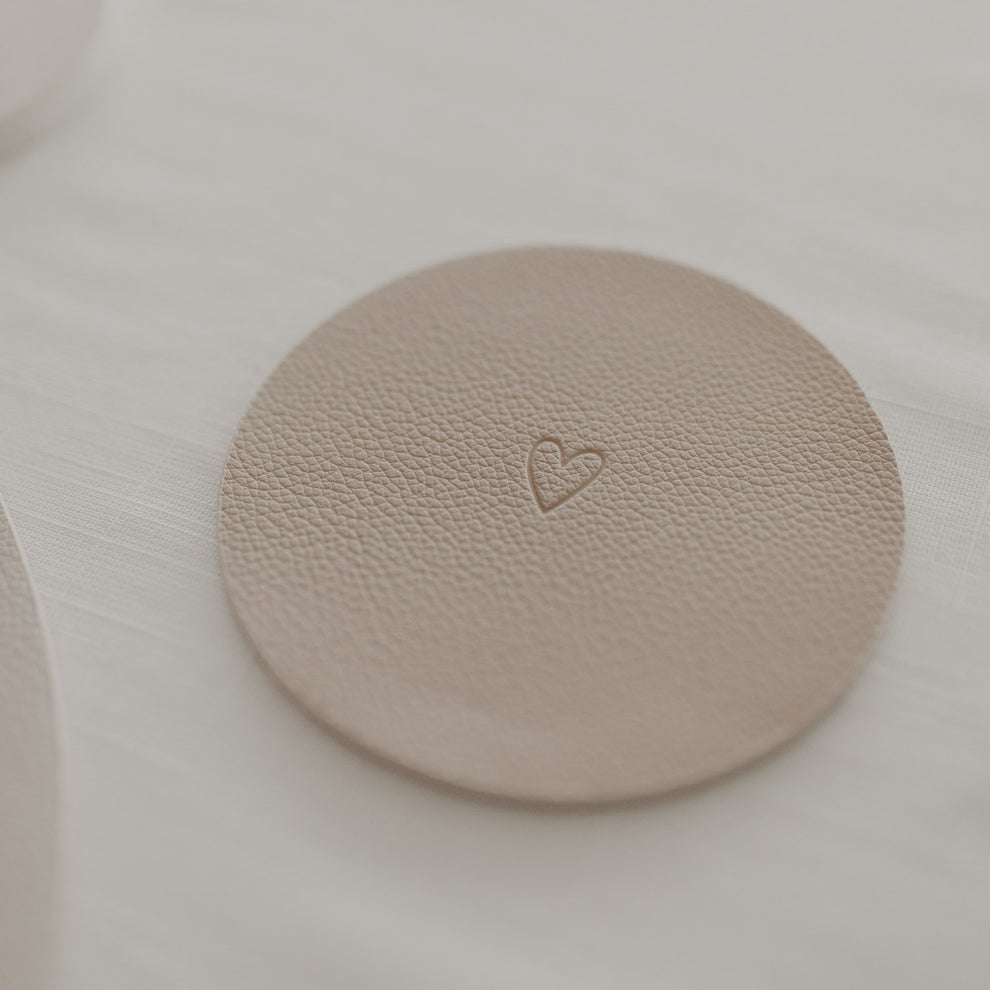 Cremefarbener Kunstleder-Untersetzer mit Herzprägung auf gedecktem Tisch in hellem Ambiente.