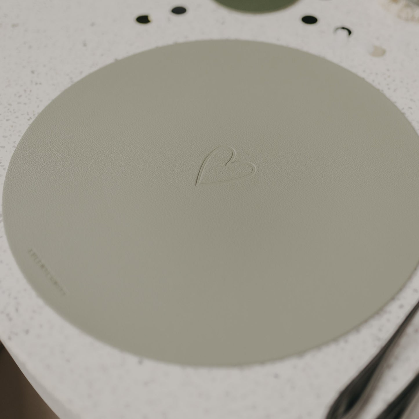 Hellgrünes Platzset Herz Grün auf Tisch, mit eingeprägtem Herzmotiv und Eulenschnitt-Logo.