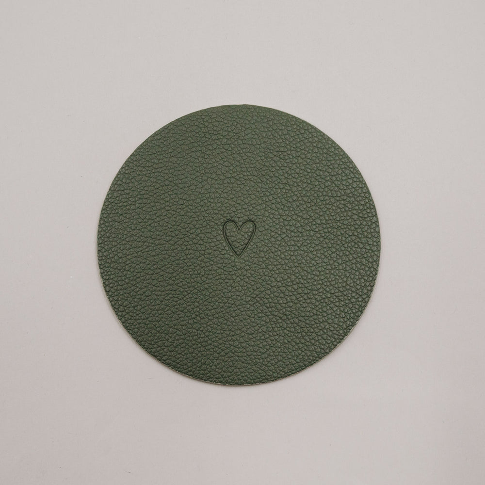 Runder grüner Untersetzer mit geprägtem Herzmotiv auf hellem Hintergrund.