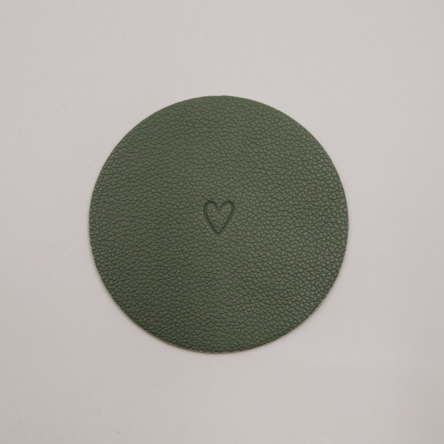 Runder grüner Untersetzer mit geprägtem Herzmotiv auf hellem Hintergrund.