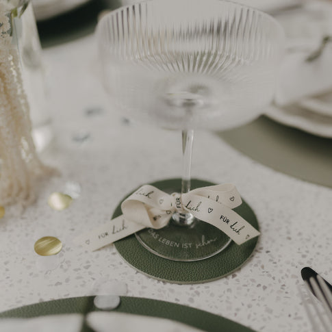 Grüner Untersetzer mit Sektglas, dekoriert mit Schleife auf Festtisch.