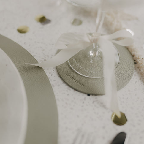 Detailaufnahme: Hellgrüner Untersetzer mit Sektglas und dekorativer Schleife.