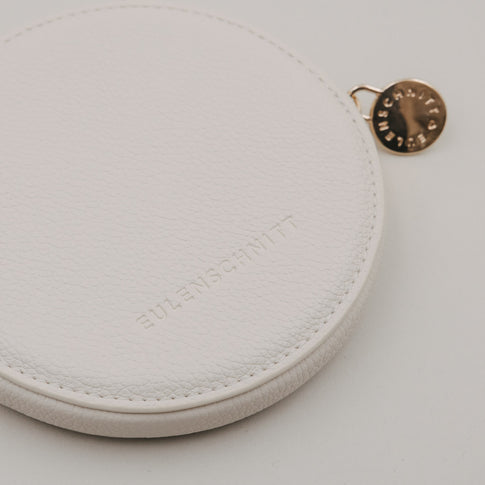 Rundes Portemonnaie in Creme mit geprägtem Eulenschnitt Logo und goldenem Reißverschlussanhänger.