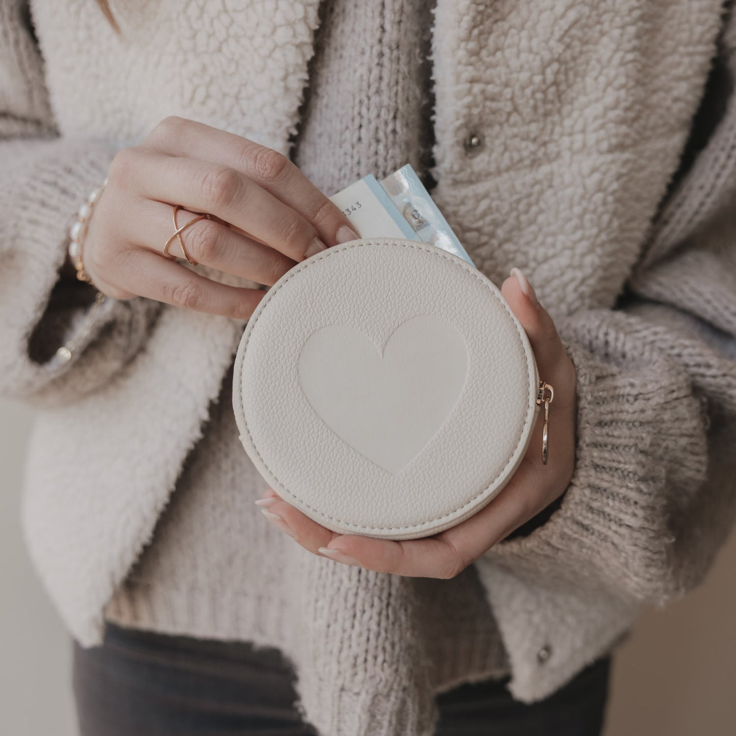 Cremefarbenes Herz-Portemonnaie in Händen, kleines rundes Etui für Münzen und Karten.