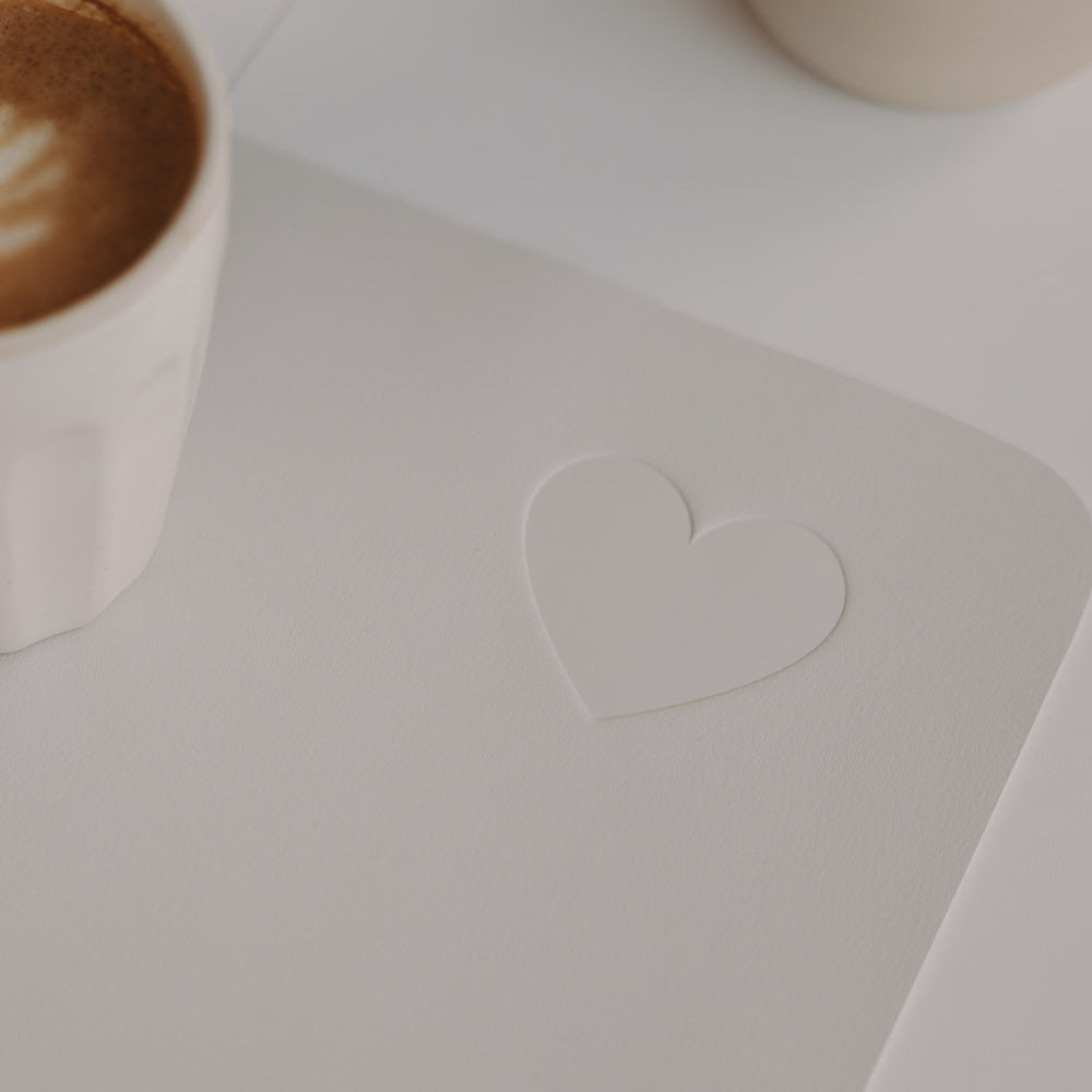 Creme Schreibtischunterlage mit Herz, Kaffeetasse im Detail auf modernem Schreibtisch