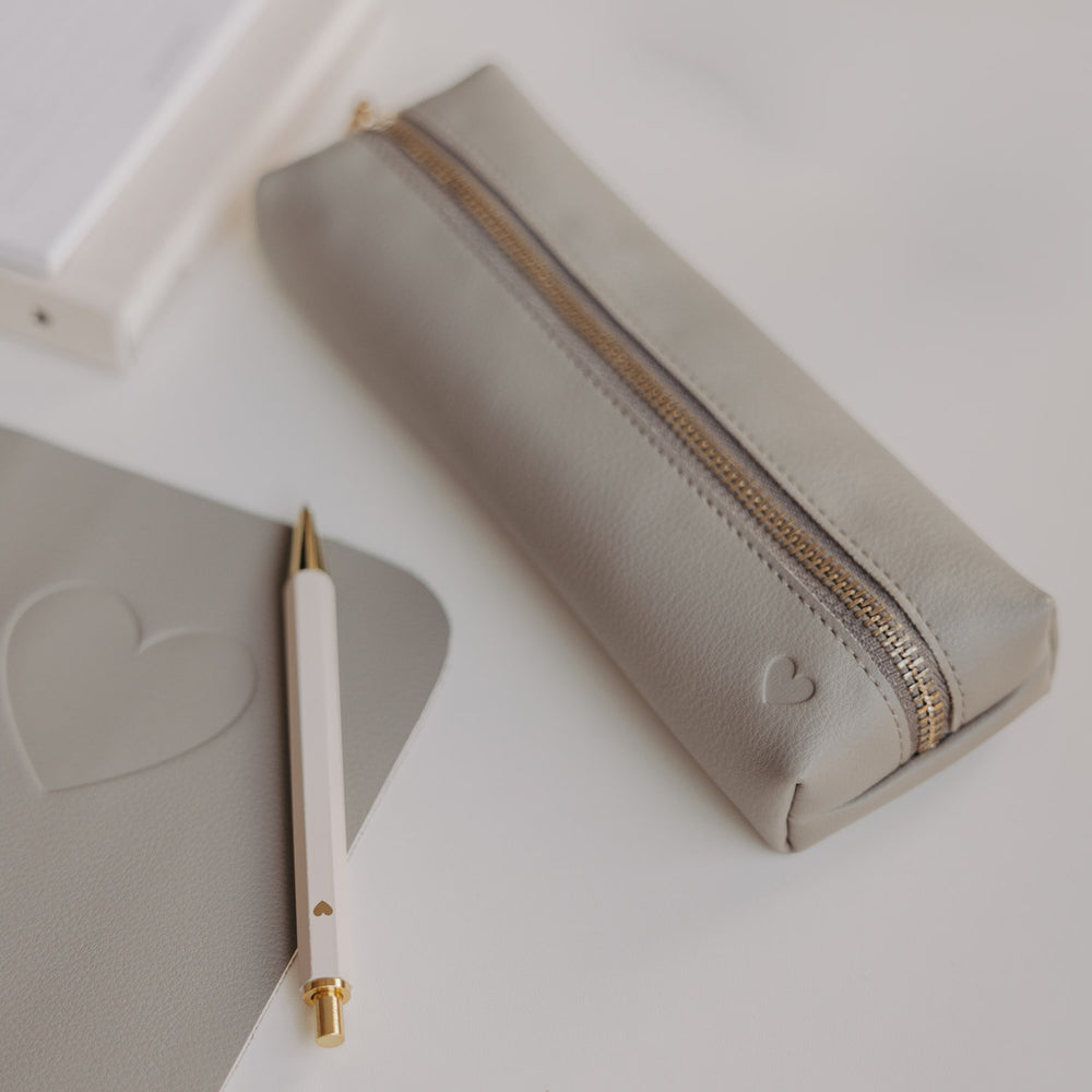 Graue Federtasche mit Herzprägung und goldenem Reißverschluss von Eulenschnitt neben Notizbuch und Stift