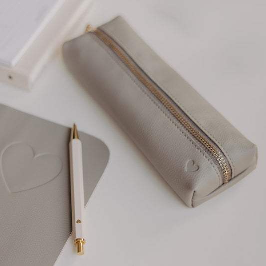 Graue Federtasche mit Herzprägung und goldenem Reißverschluss von Eulenschnitt neben Notizbuch und Stift