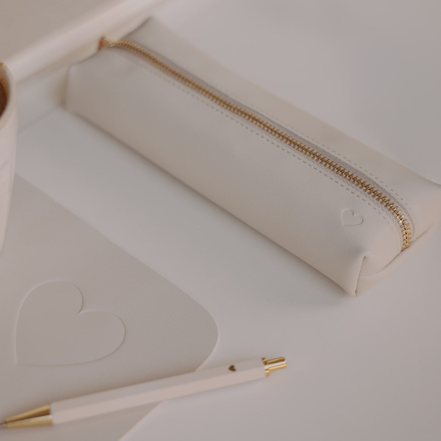 Federtasche creme mit Herzprägung und goldenem Reißverschluss von Eulenschnitt neben Notizbuch und Stift