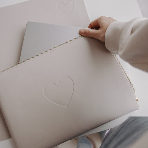 Hand hält taupefarbene Laptophülle mit Herzprägung vor Laptop