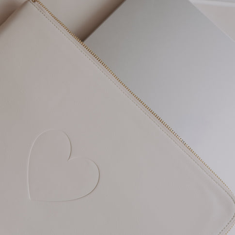 Cremefarbene Laptophülle mit Herzprägung neben Laptop auf hellem Schreibtisch