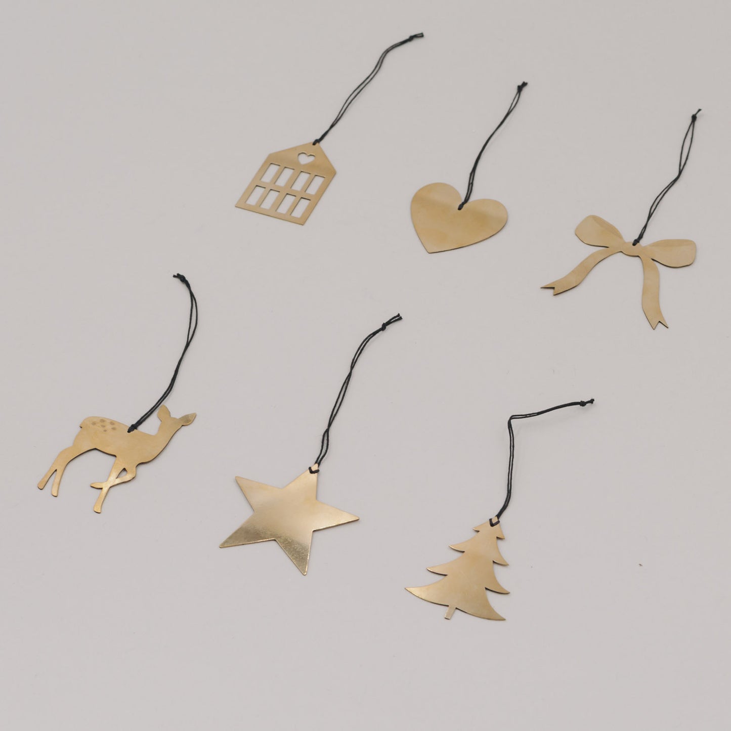 Goldene Anhänger Herz, Stern, Haus, Schleife, Reh und Tanne locker arrangiert auf weißem Untergrund.