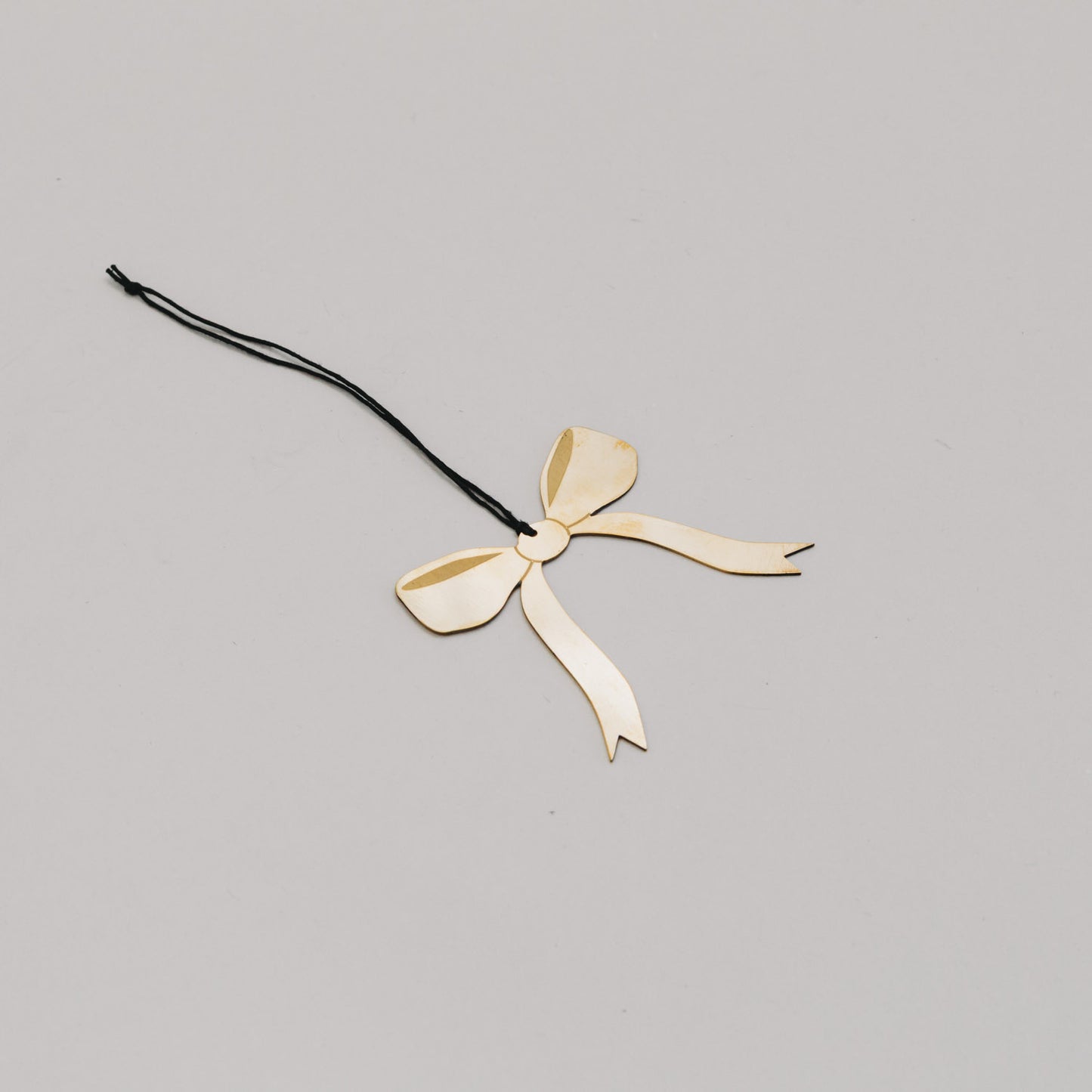 Goldene Schleife aus Metall in schräger Perspektive, filigran gearbeitet mit schwarzer Aufhängung.