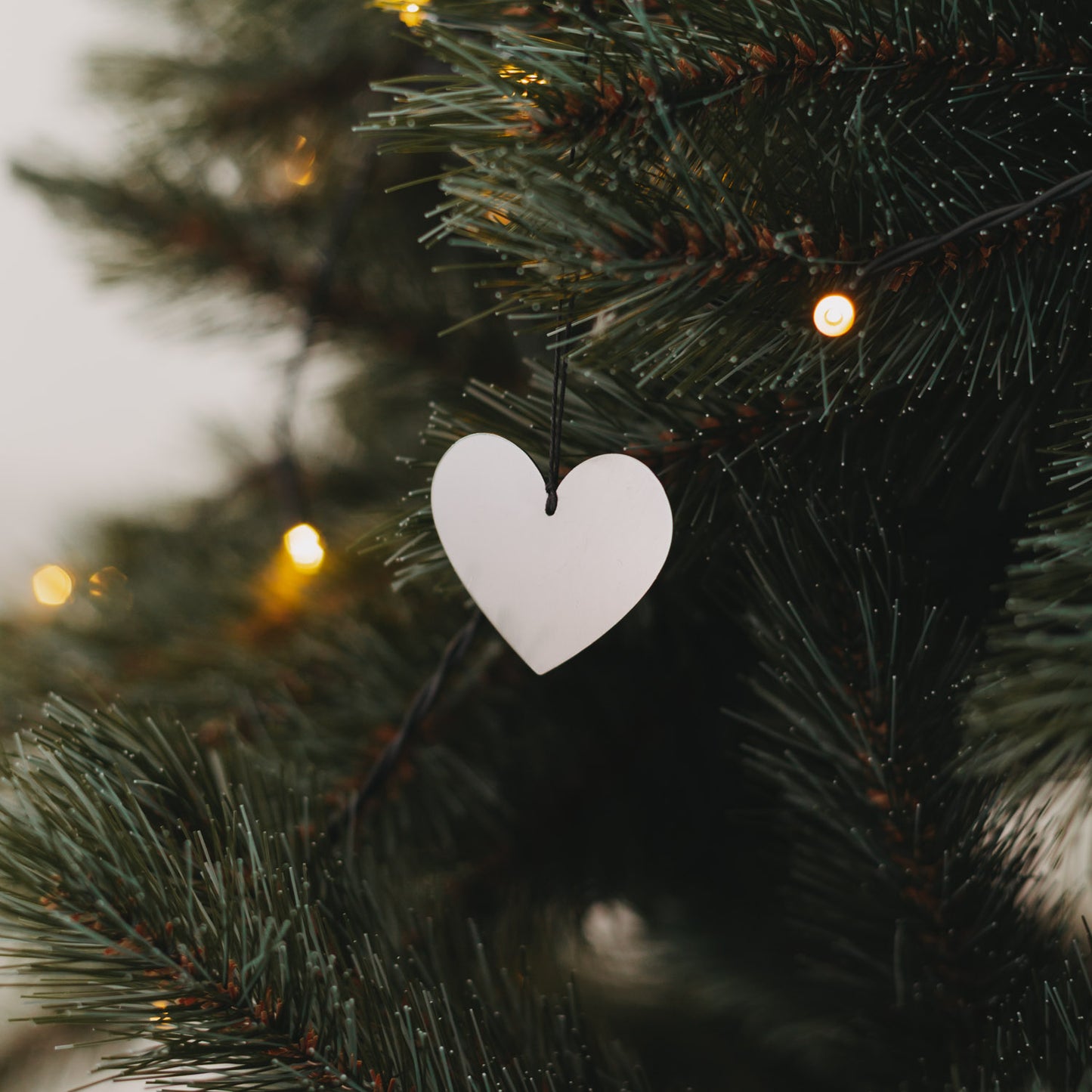 Glänzender Herzanhänger aus Metall in Silber – dekorativ am Tannenbaum befestigt mit schwarzem Band