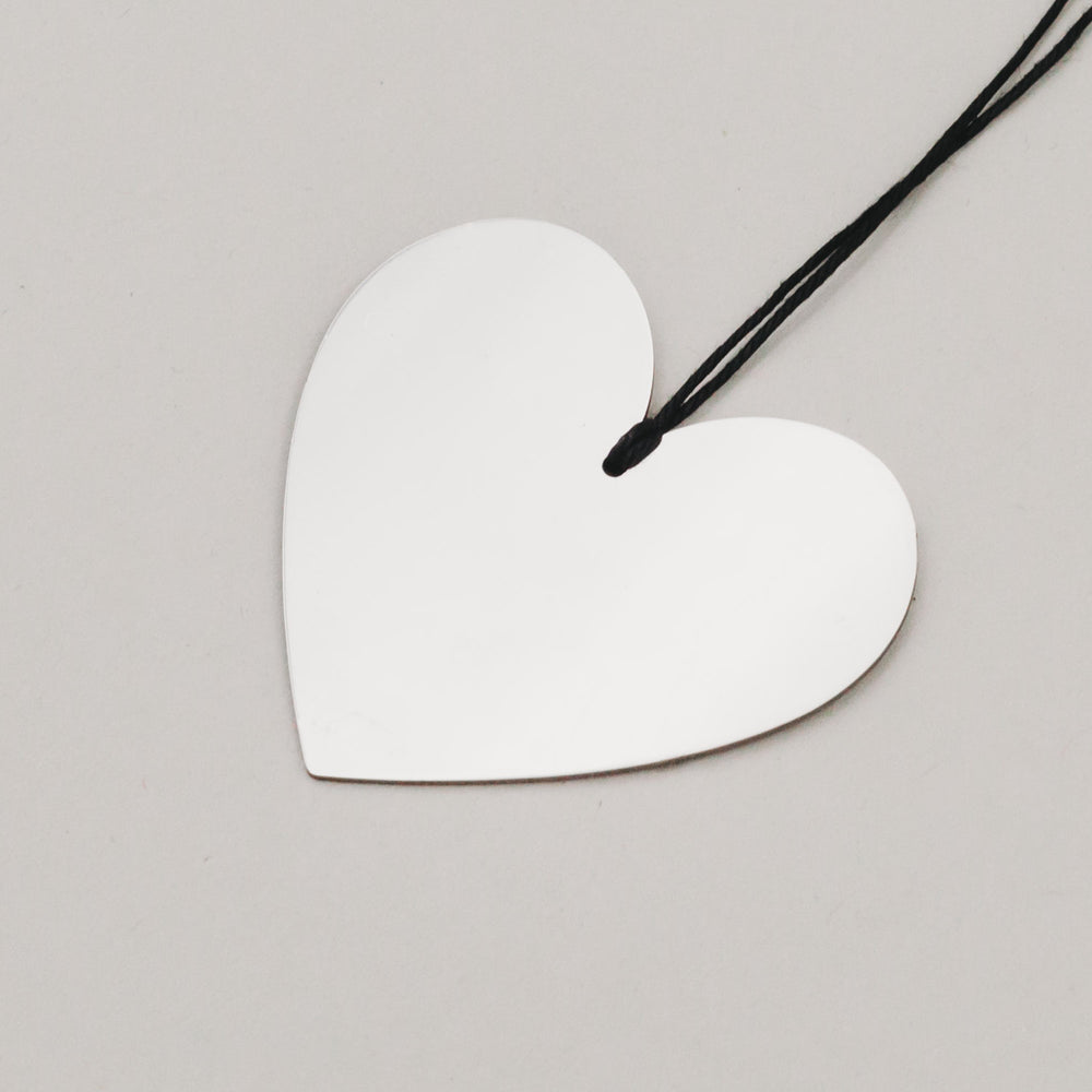 Detailaufnahme eines silbernen Herzanhängers aus Metall mit schwarzer Aufhängung