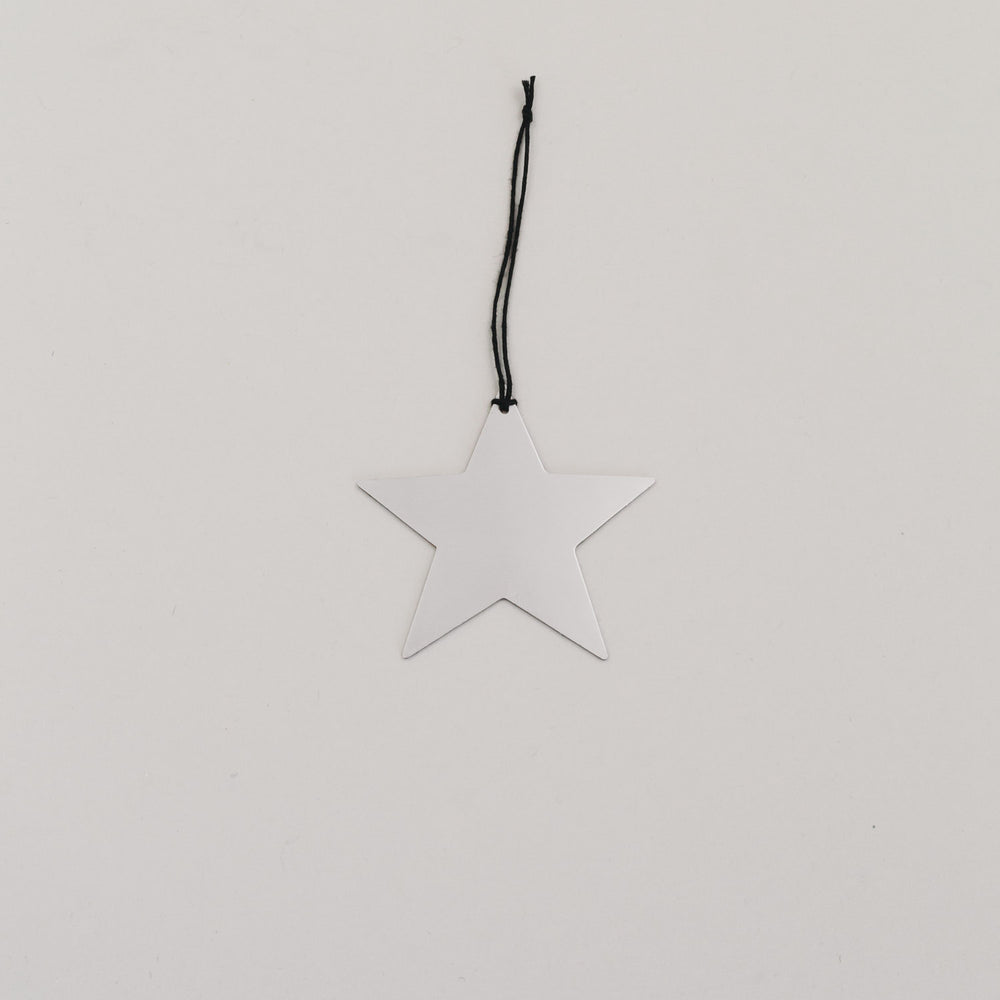 Silberner Sternanhänger aus Metall mit schwarzer Kordel auf hellem Hintergrund, minimalistisch arrangiert.
